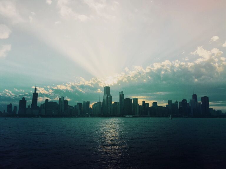 city skyline with sun and clouds with water in front